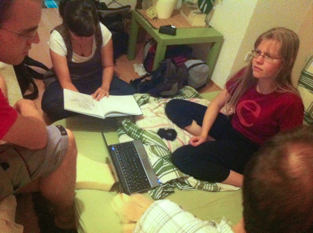 Henrieke, Titash and me sitting on the floor of our hosts apartment and showing a sketchbook to our host.