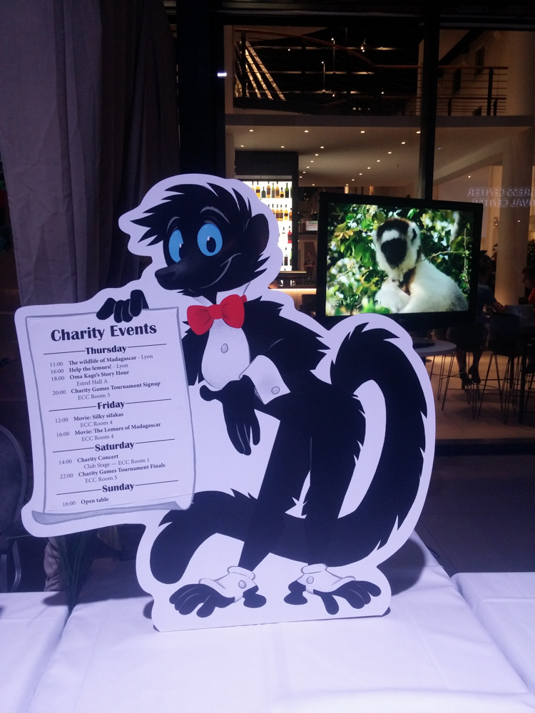 A standee of a cartoony blue-eyed black lemur presenting the charity schedule, drawn by Henrieke